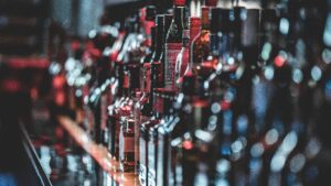 Blurred view of assorted alcohol bottles lined up on a bar shelf indoors.