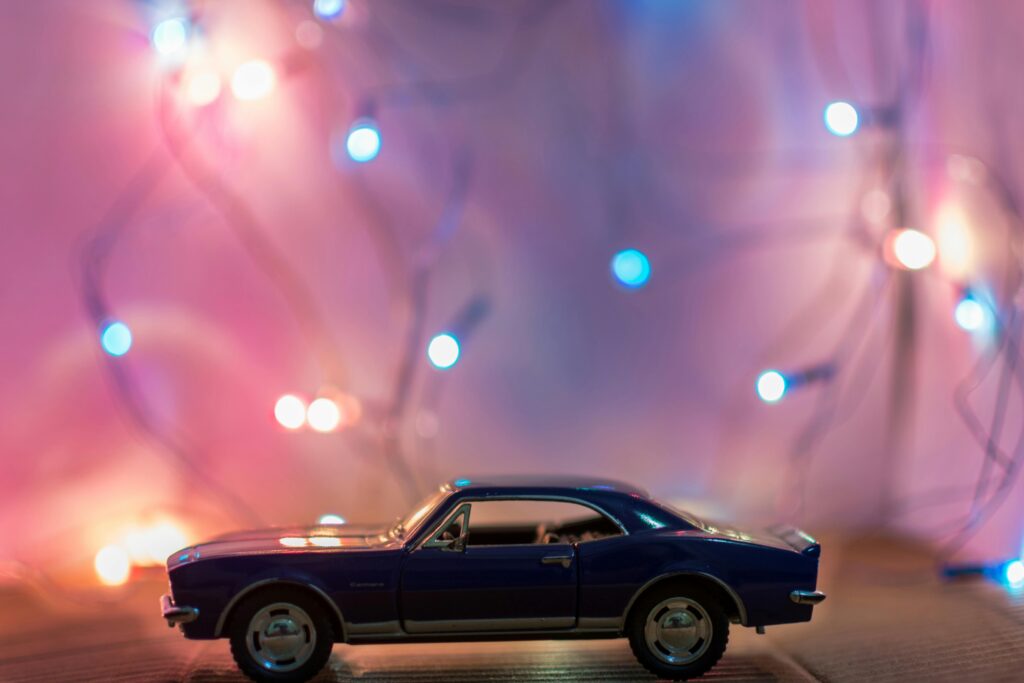 A miniature toy car in front of colorful festive lights creating a bokeh effect.